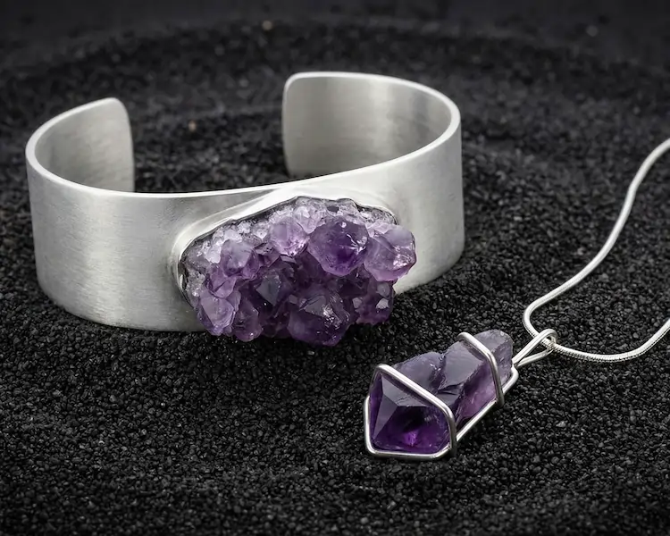 Architectural jewelry featuring raw mineral crystals like pyrite and quartz, secured in heavy silver claw settings with industrial finishes, displayed on a slate background.